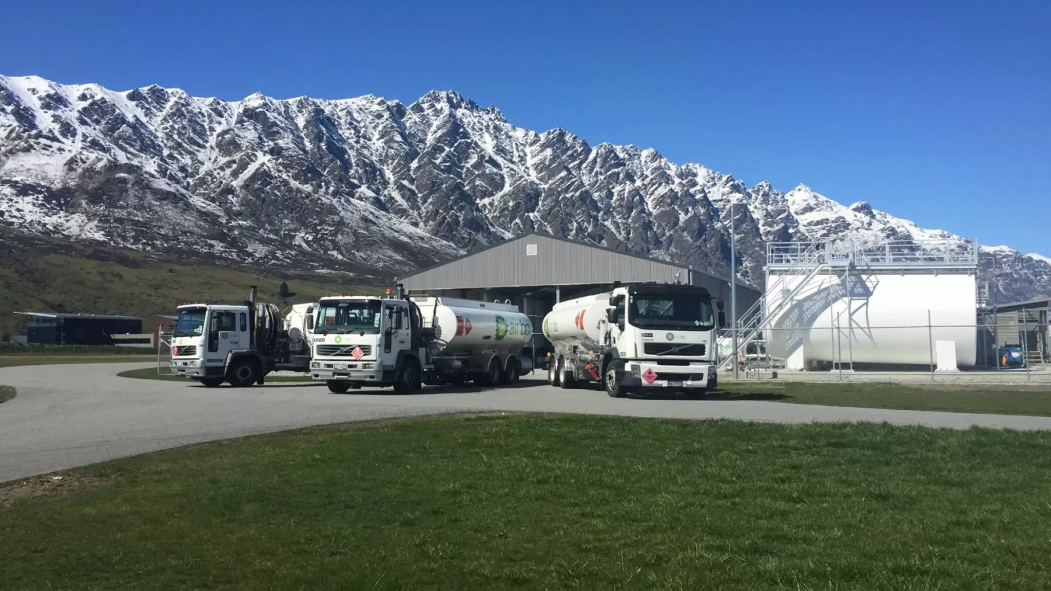 Three fuel tankers in front of snow-capped mountains near a depot