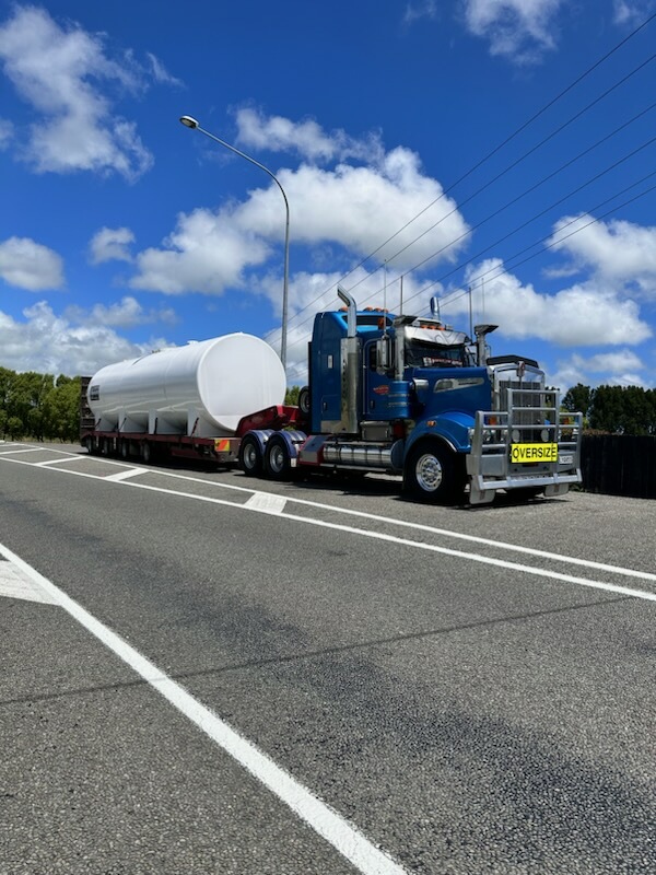 Truck carrying a white tank on a trailer along a road
