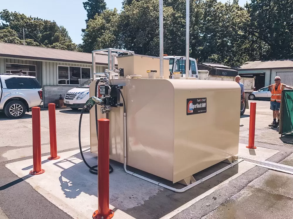 Beige SuperVault tank with a pump behind red bollards at a depot