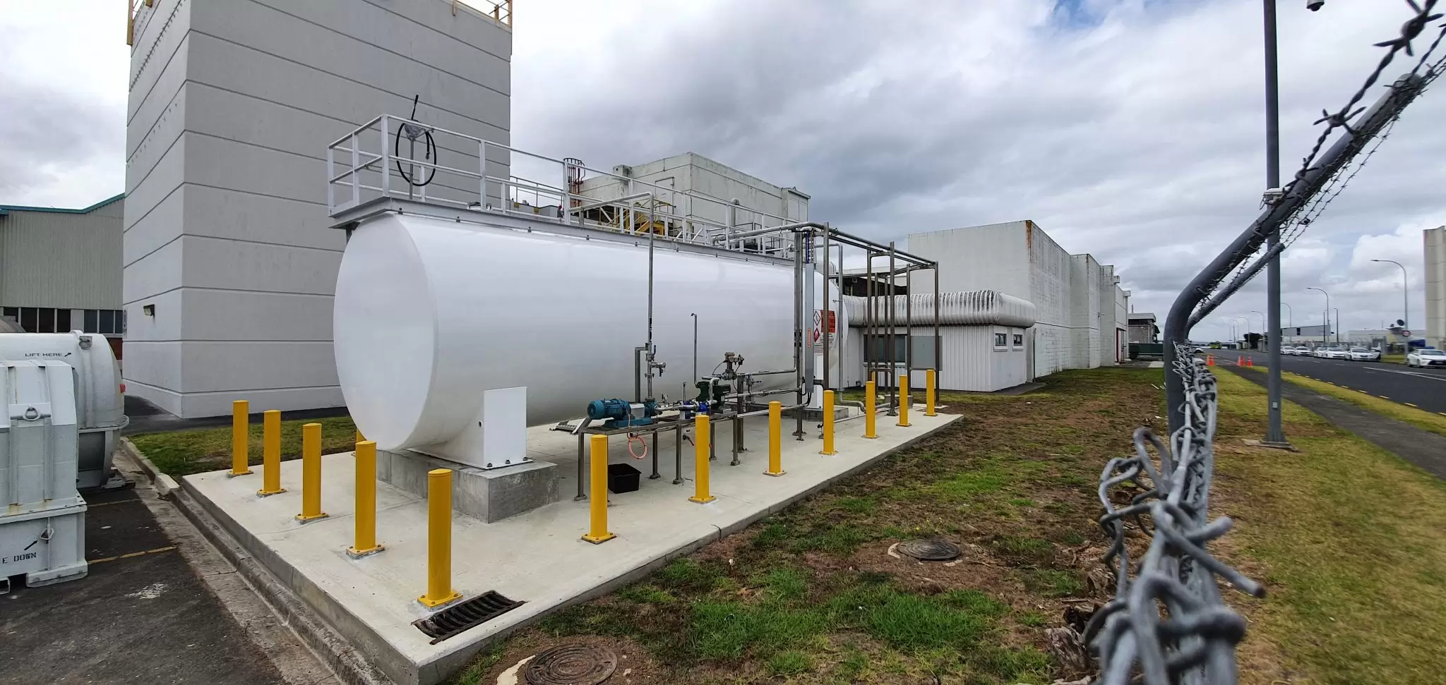 Large white horizontal fuel tank behind yellow bollards beside a building