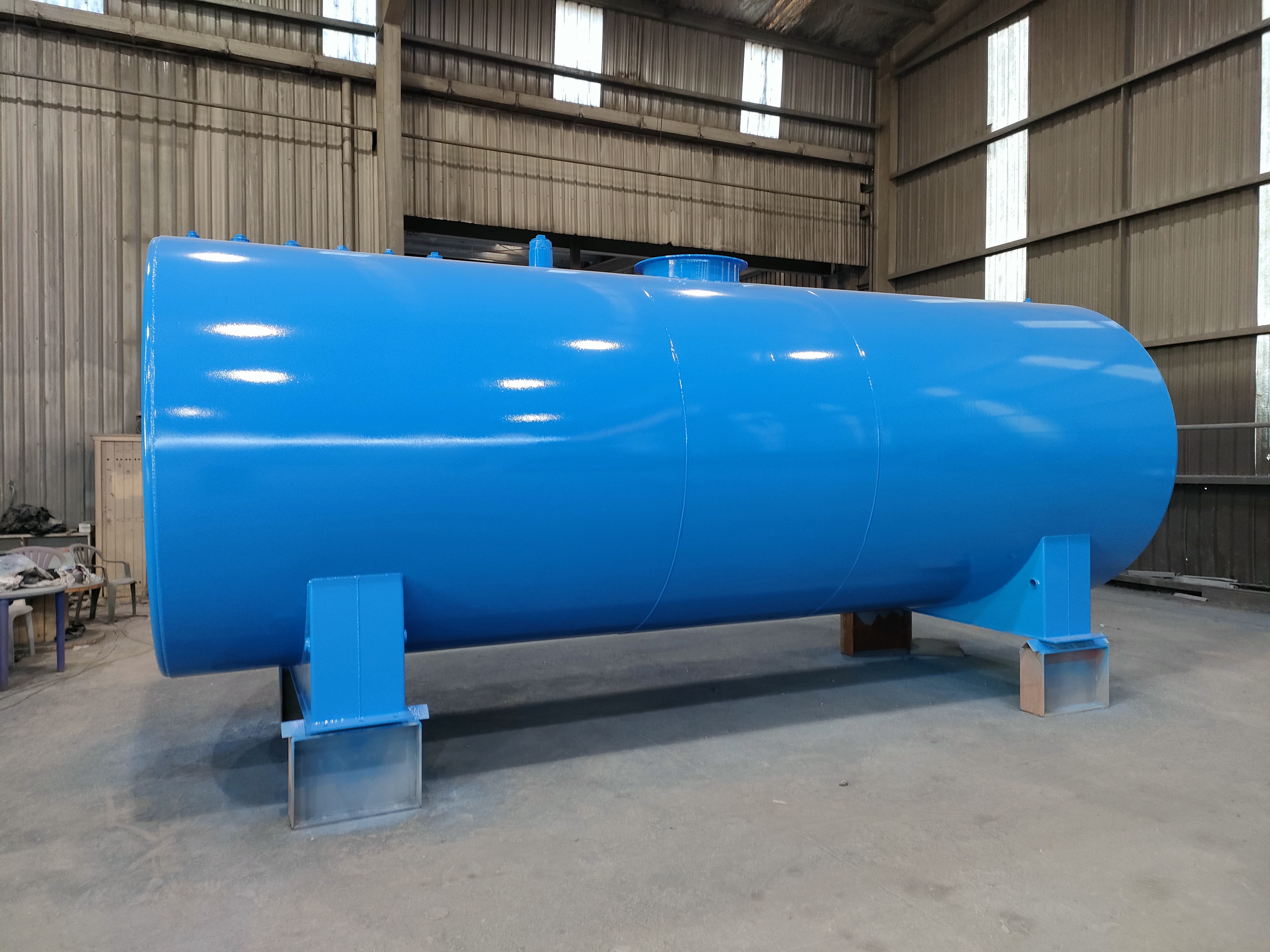 Bright blue horizontal fuel tank on steel stands in a factory