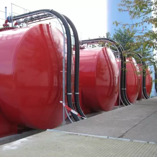 Row of red tanks with black pipework beside a path