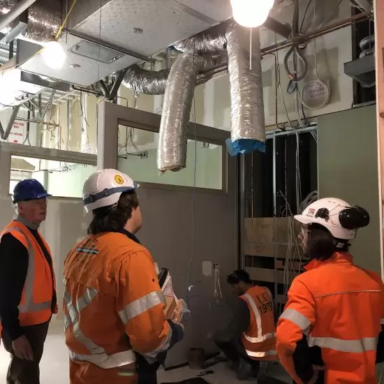 Four workers in hard hats and high-vis clothing inspecting a building plant room