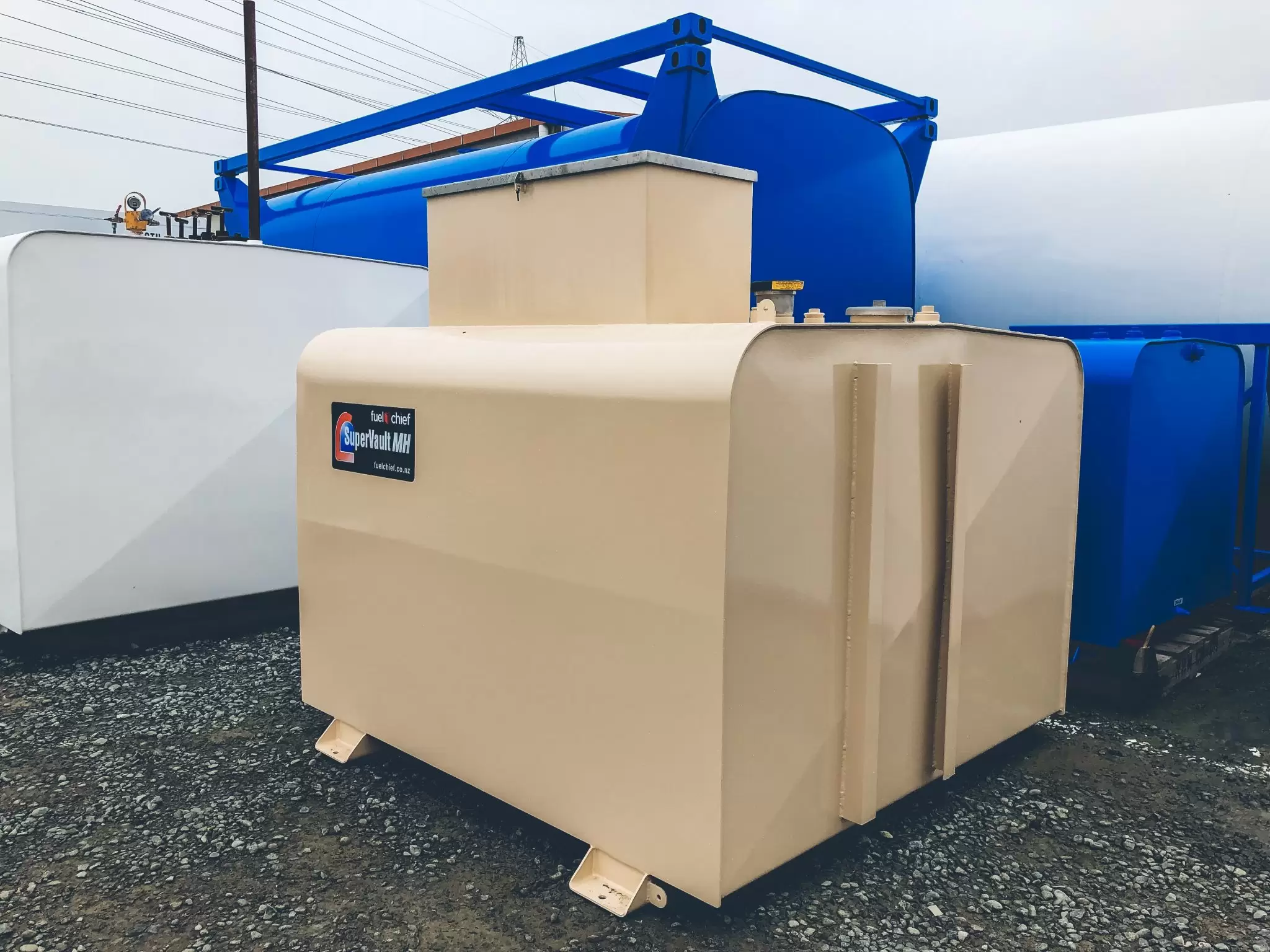 Beige SuperVault tank beside blue and white tanks on a gravel yard