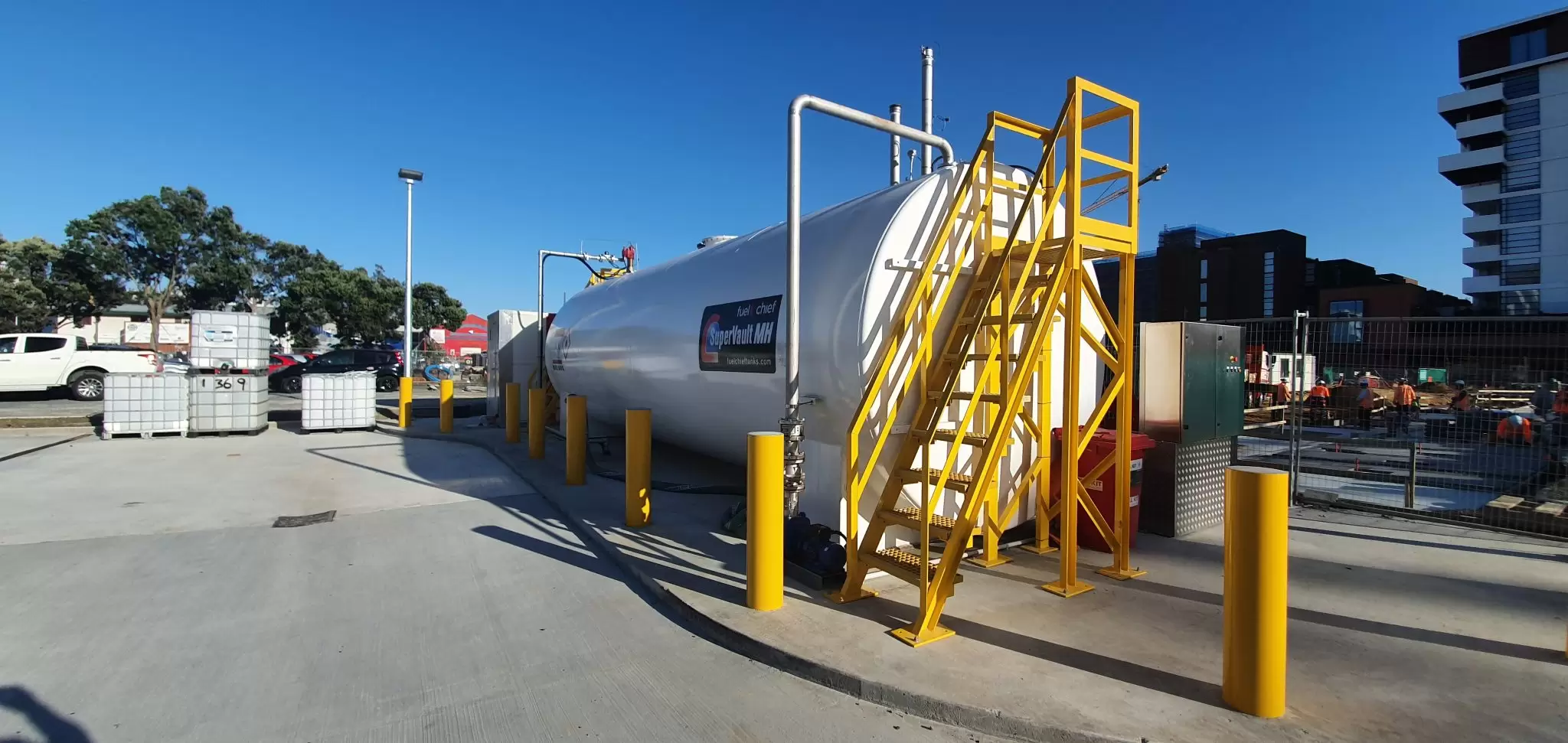 White tank with yellow stairs and bollards at a bus depot
